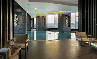 Una piscina interna moderna con pareti in pietra e ampie finestre che offrono vista sulla città.