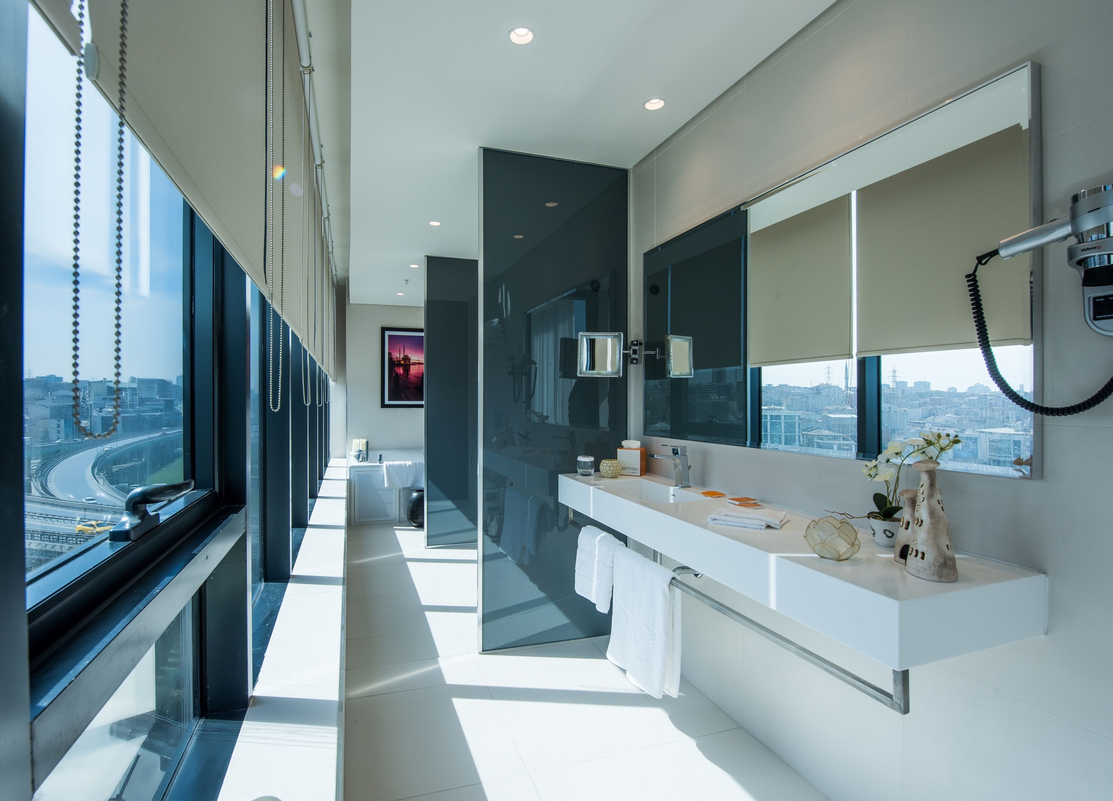Un baño moderno con un espejo grande, un tocador con lavamanos y vistas a la ciudad desde la ventana.
