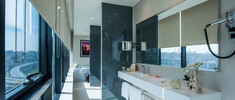 Un baño moderno con un espejo grande, un tocador con lavamanos y vistas a la ciudad desde la ventana.