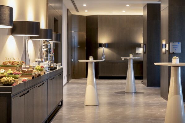 A modern hotel lobby with a buffet area, a meeting room, and a reception desk.