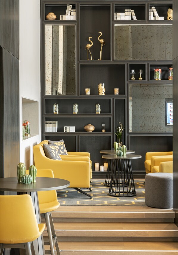 En moderne stue med sofa, gule stole, sofabord og reol med pynt.