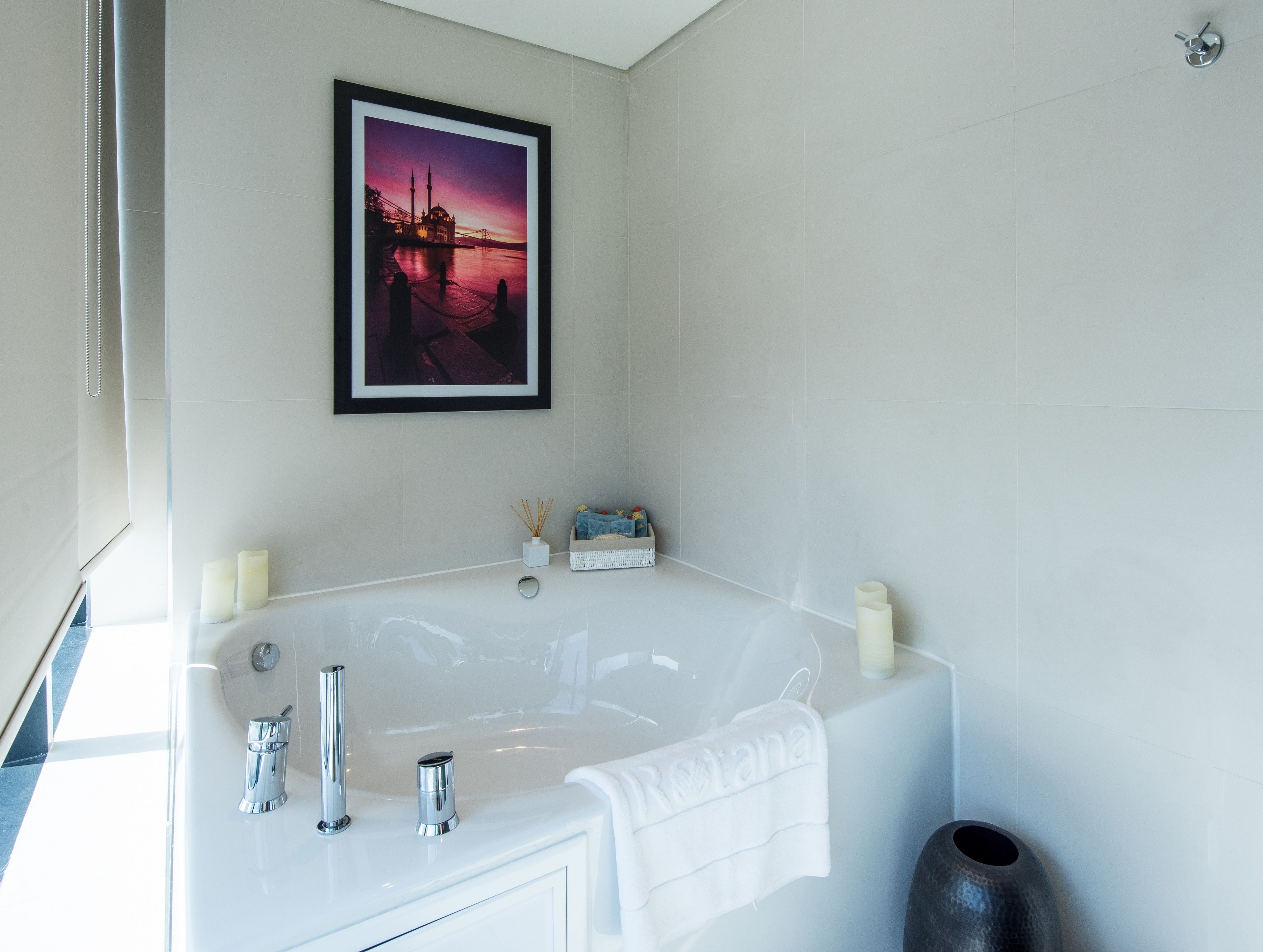Ein modernes Badezimmer mit einer großen Badewanne, einem gerahmten Bild von einem Sonnenuntergang und einem kleinen Korb mit Toilettenartikeln.