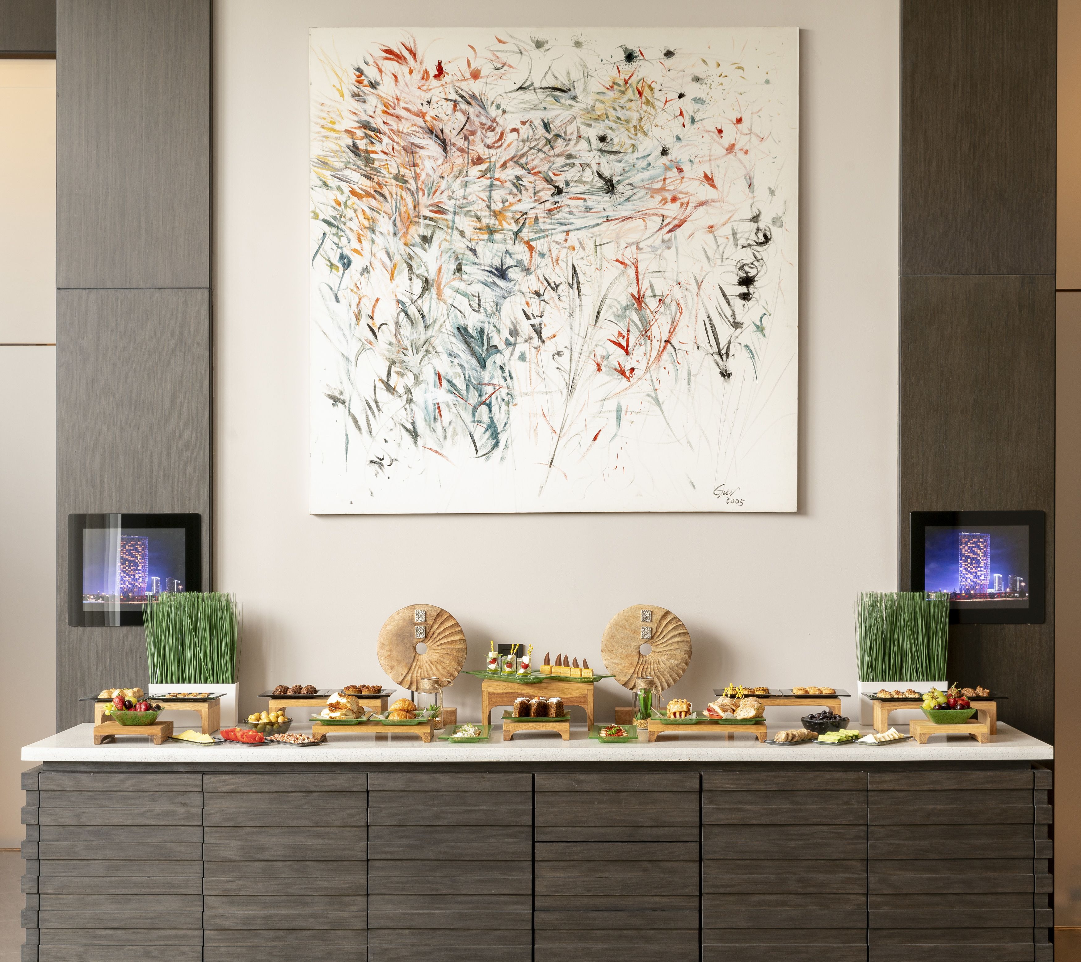 Uma cozinha moderna com uma grande pintura abstrata, dois monitores digitais e diversos alimentos sobre o balcão.