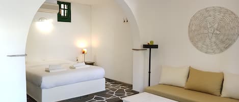 A hotel room with a bed, a sofa, a coffee table, a wall-mounted lamp, a decorative wall piece, and a tiled floor.