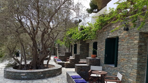 Un espace extérieur aménagé avec des murs en pierre, doté de bancs et de tables intégrés, et entouré d’arbres et d’un sentier en pierre.