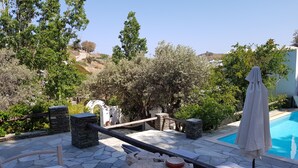 Un espace aménagé au bord de la piscine, avec un sol en pierre, une table en bois, un parasol blanc et une vue sur le paysage environnant.