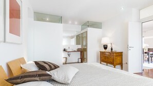 A modern bedroom with a large bed, a wooden dresser, a mirror, and a bathroom visible through an open door. - Design Apartments mit Terrasse - Adults Only (Innsbruck)