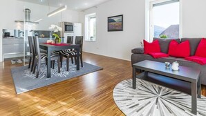 A modern living room with a sofa, a dining table with chairs, and a kitchen area in the background. - Design Apartments mit Terrasse - Adults Only (Innsbruck)