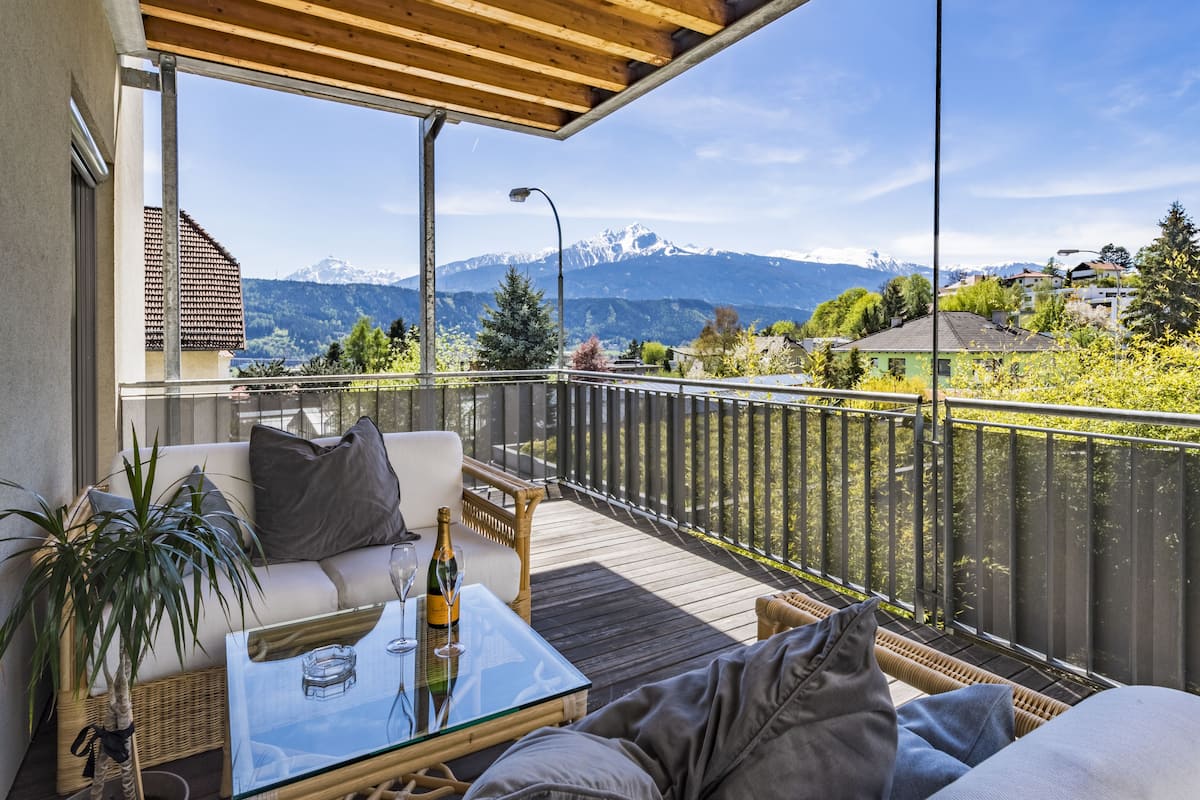 Un balcon avec une table en verre, des meubles en osier et une vue sur les montagnes.