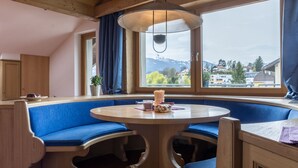 A cozy room with a round wooden table, blue cushioned seating, and a large window offering a mountain view. - Design Apartments mit Terrasse - Adults Only (Innsbruck)