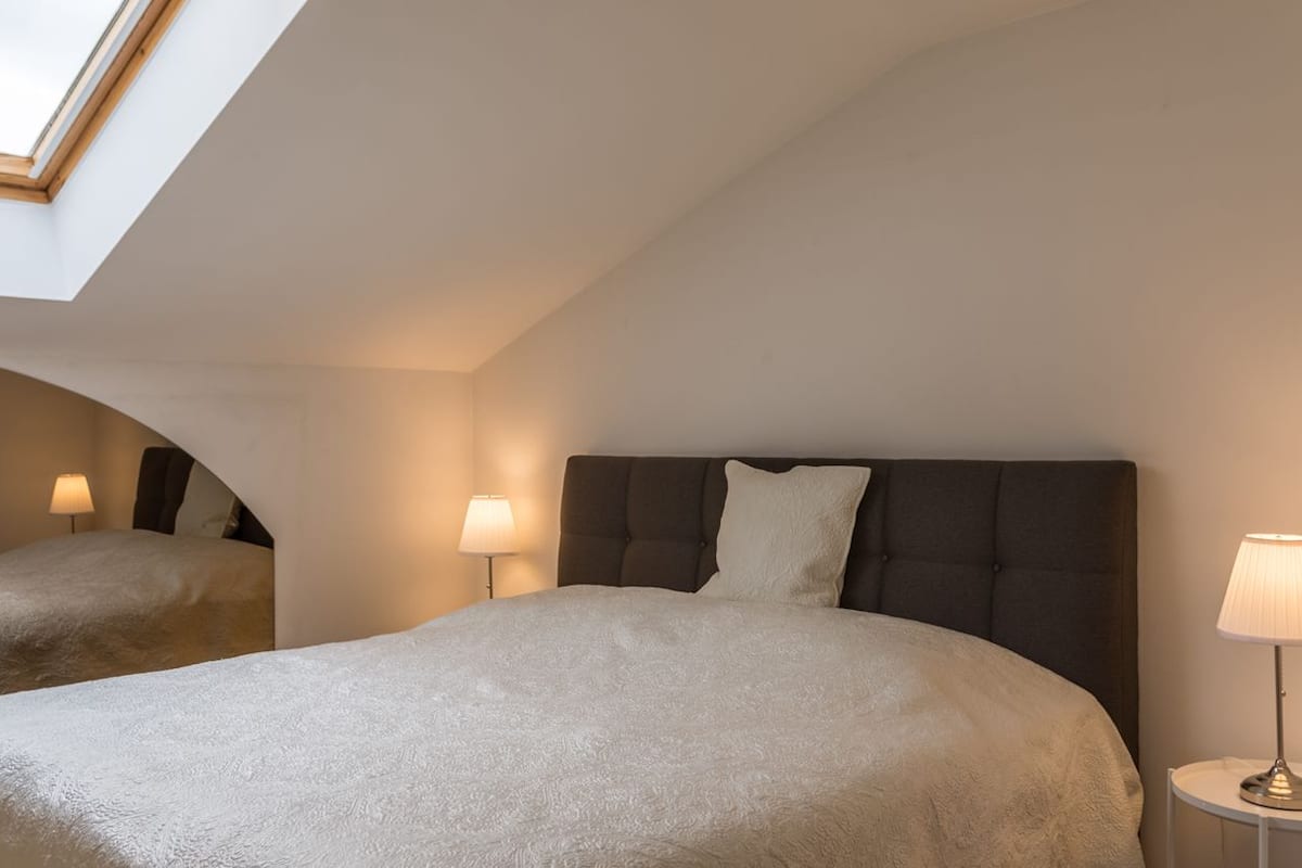 Une chambre avec deux lits, une lucarne et des lampes de chevet.
