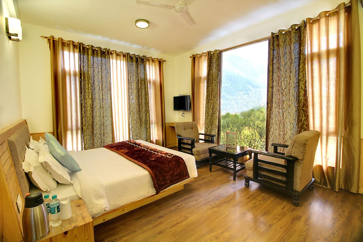 A hotel room with a bed, two armchairs, a small table, a television, and a view of the outdoors.