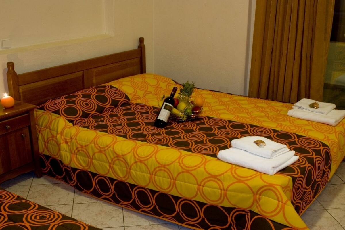 Ein Hotelzimmer mit einem hölzernen Bett, einem Nachttisch mit einer Lampe und einer Obstschale auf dem Bett.