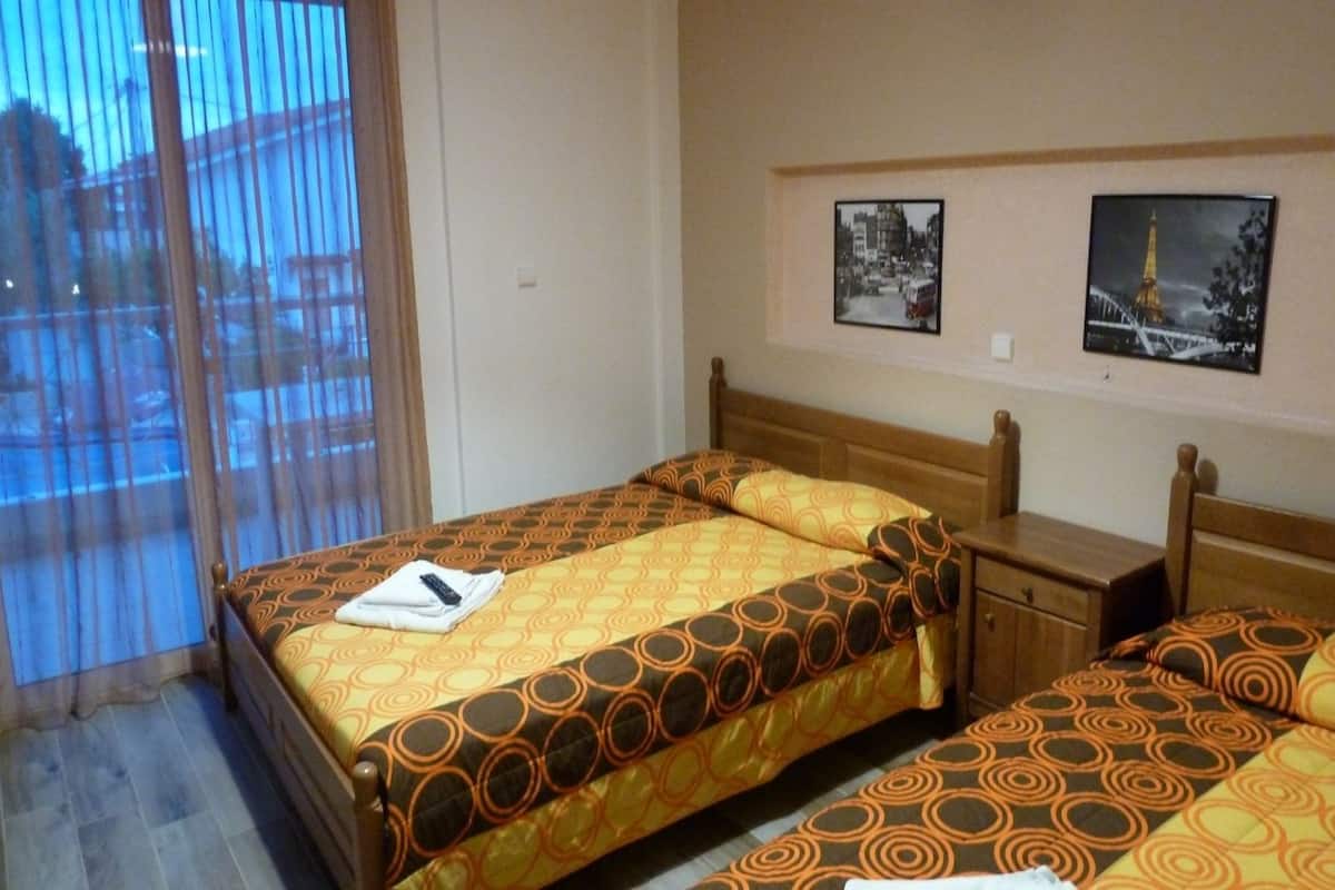 Ein Hotelzimmer mit zwei Betten, einem Holzkopfteil, einem kleinen Nachttisch und einem Fenster mit Vorhängen.