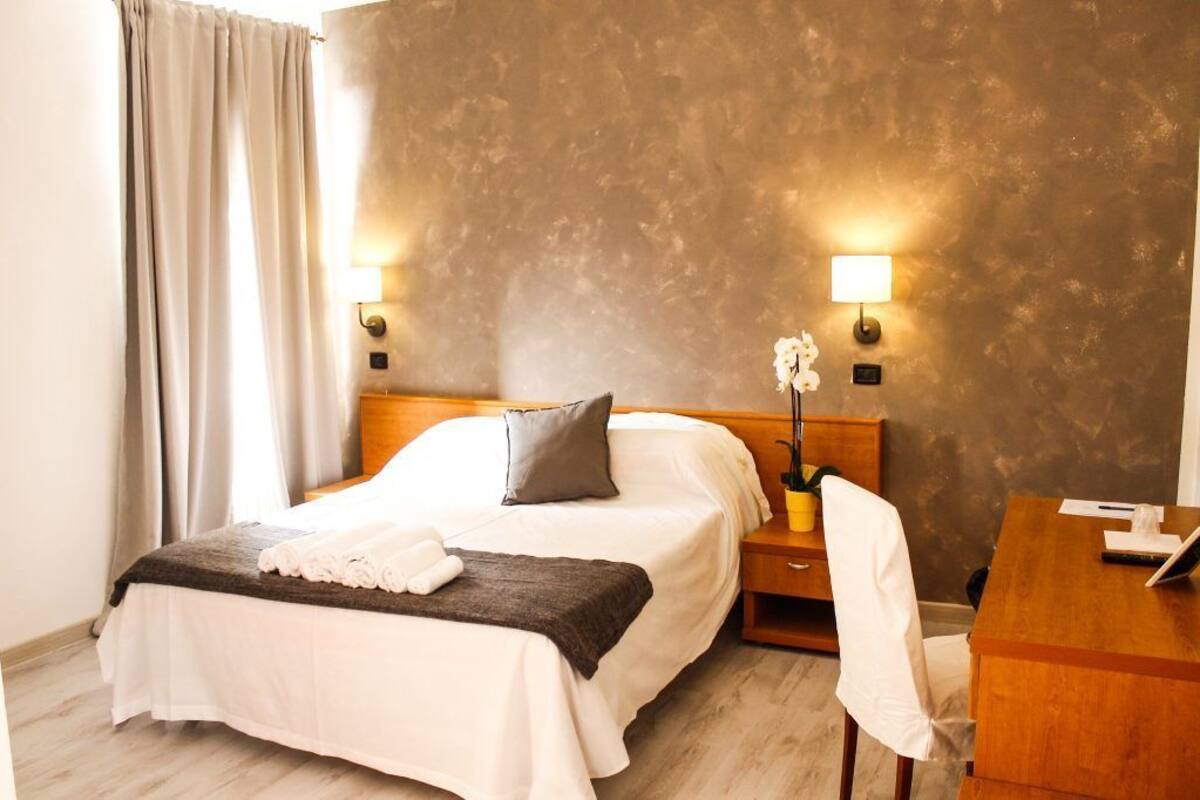 A hotel room with a bed, bedside tables, a desk, and a chair.