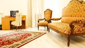 A room with a wooden desk, a television, a patterned sofa, a chair, and a red and beige carpet. - Aquam Albergo (Acqui Terme)