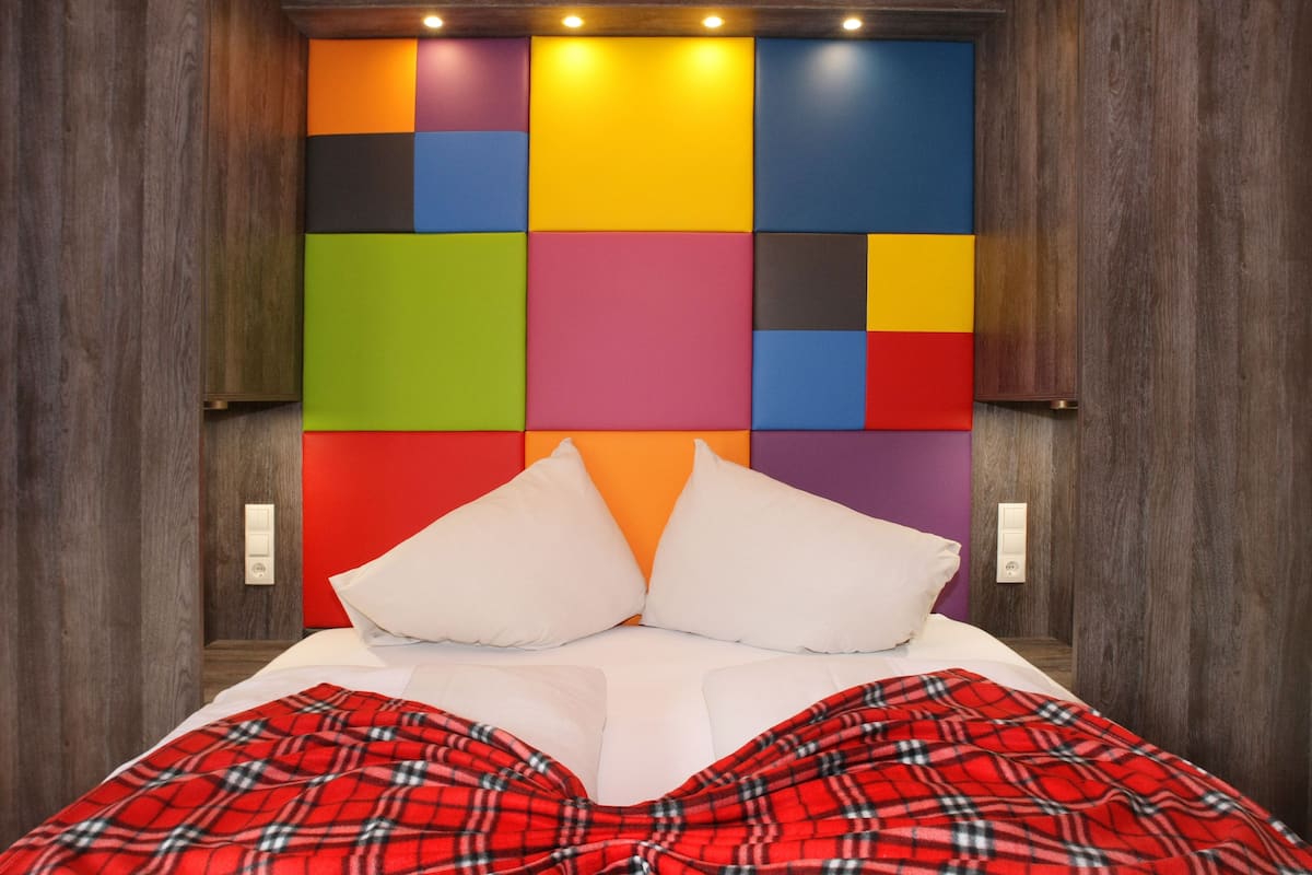 A bed with a colorful headboard, white pillows, and a red plaid blanket.
