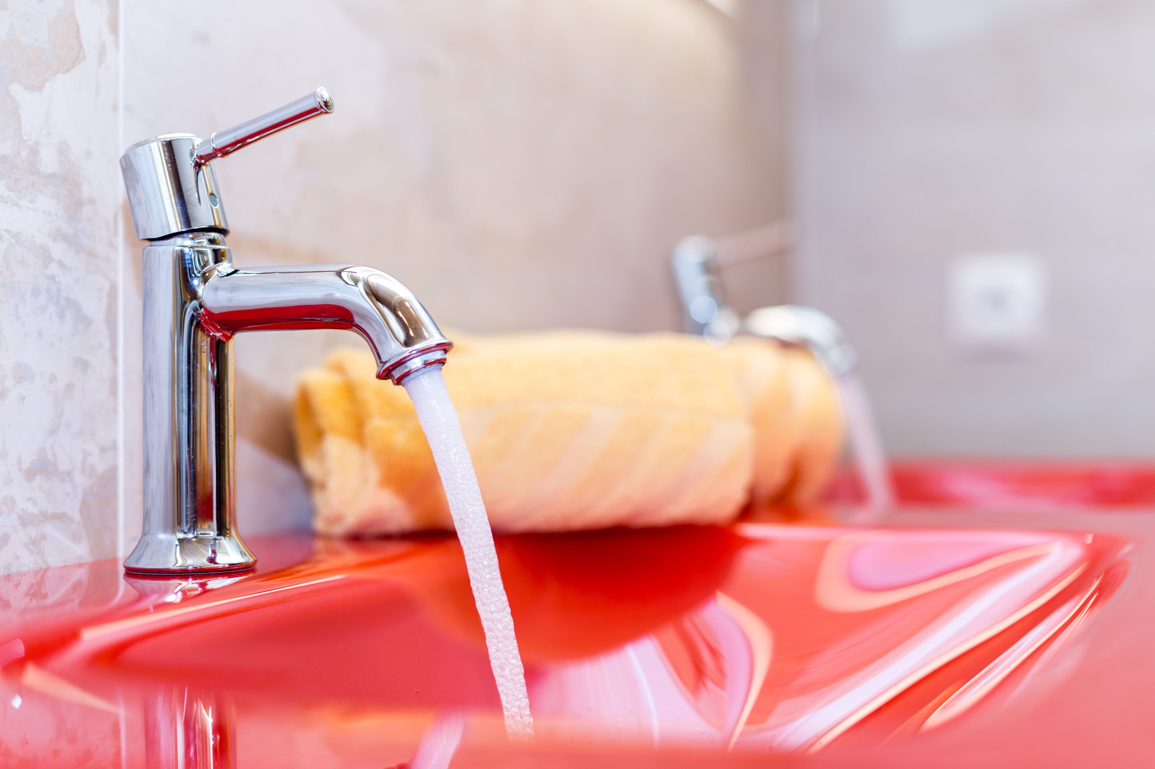A bathroom with a chrome faucet, a towel, and a red sink.
