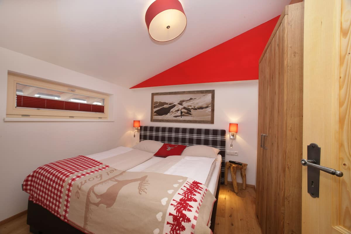 A bedroom with a bed, a window with blinds, a painting on the wall, and a wooden door.