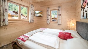 A wooden cabin room with a bed, two windows, a TV, and a painting. - The Kaprun Edition (Kaprun)