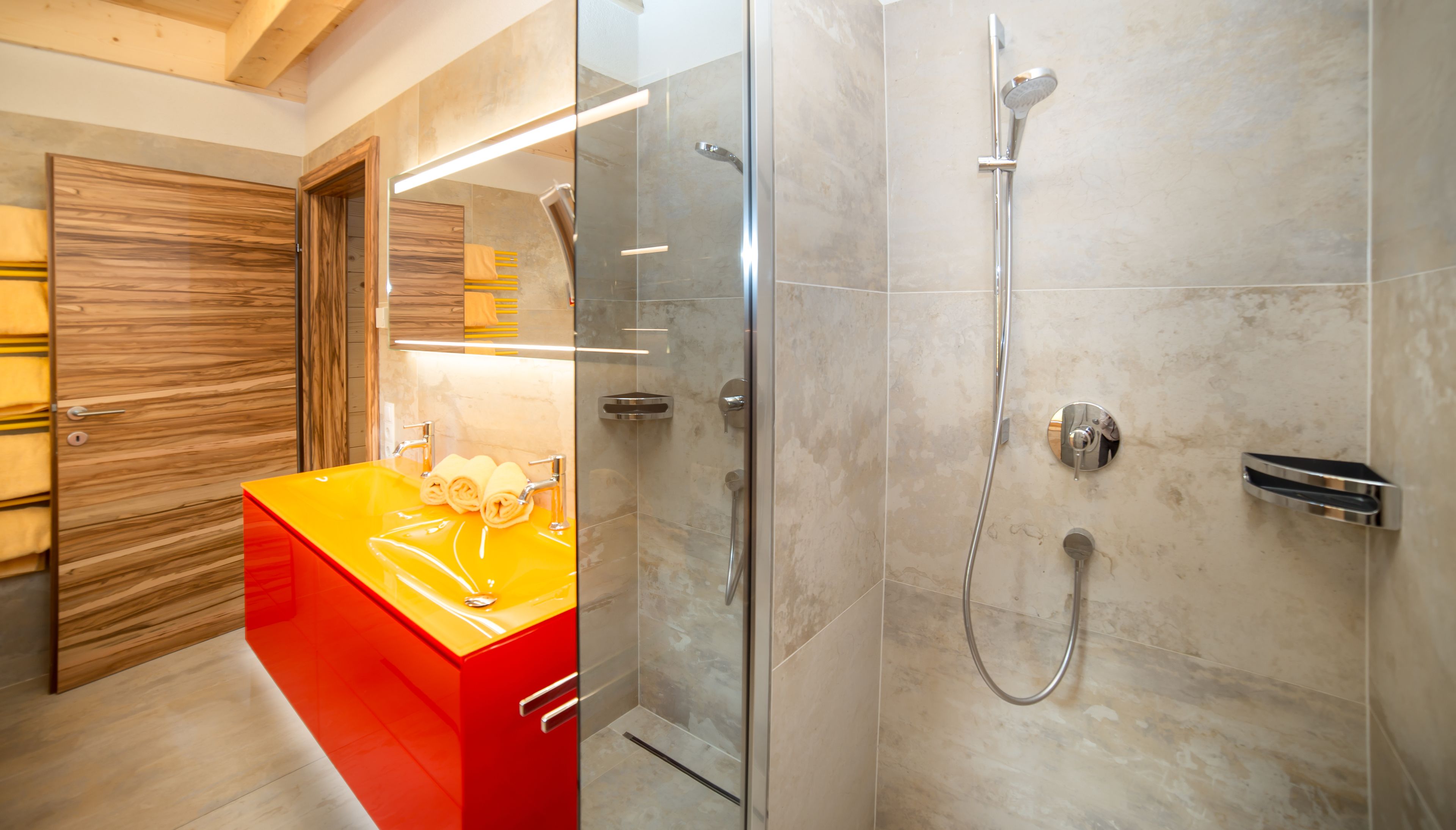 Ein modernes Badezimmer mit einer gläsernen Duschkabine, einem roten Waschtisch und einer Holztür.
