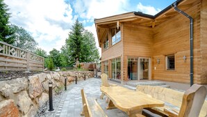 A wooden building with a patio area featuring benches and a table. - The Kaprun Edition (Kaprun)