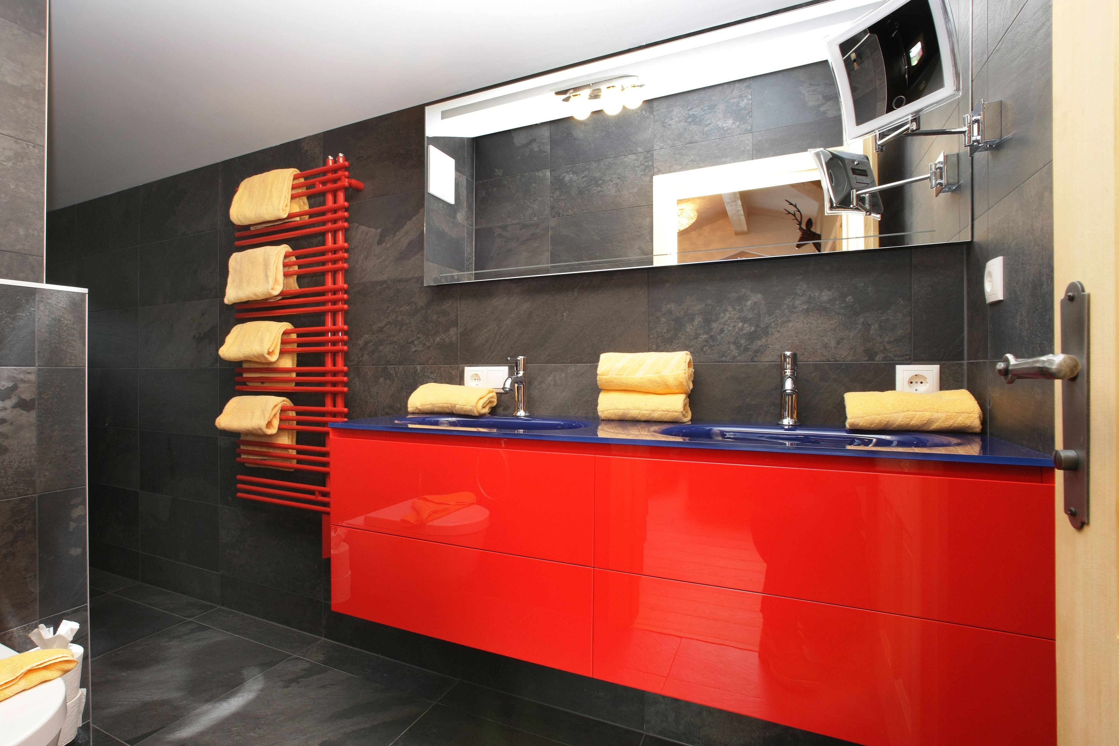 A modern bathroom with a red vanity, a mirror, and a towel rack with multiple towels.