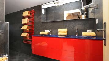 A modern bathroom with a red vanity, a mirror, and a towel rack with multiple towels.