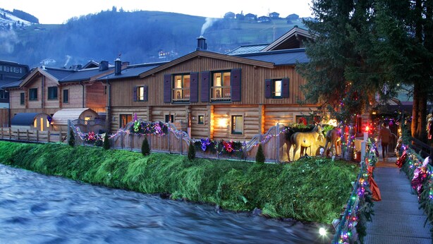 A log cabin-style hotel with a river in front, decorated with festive lights and garlands. - The Kaprun Edition (Kaprun)