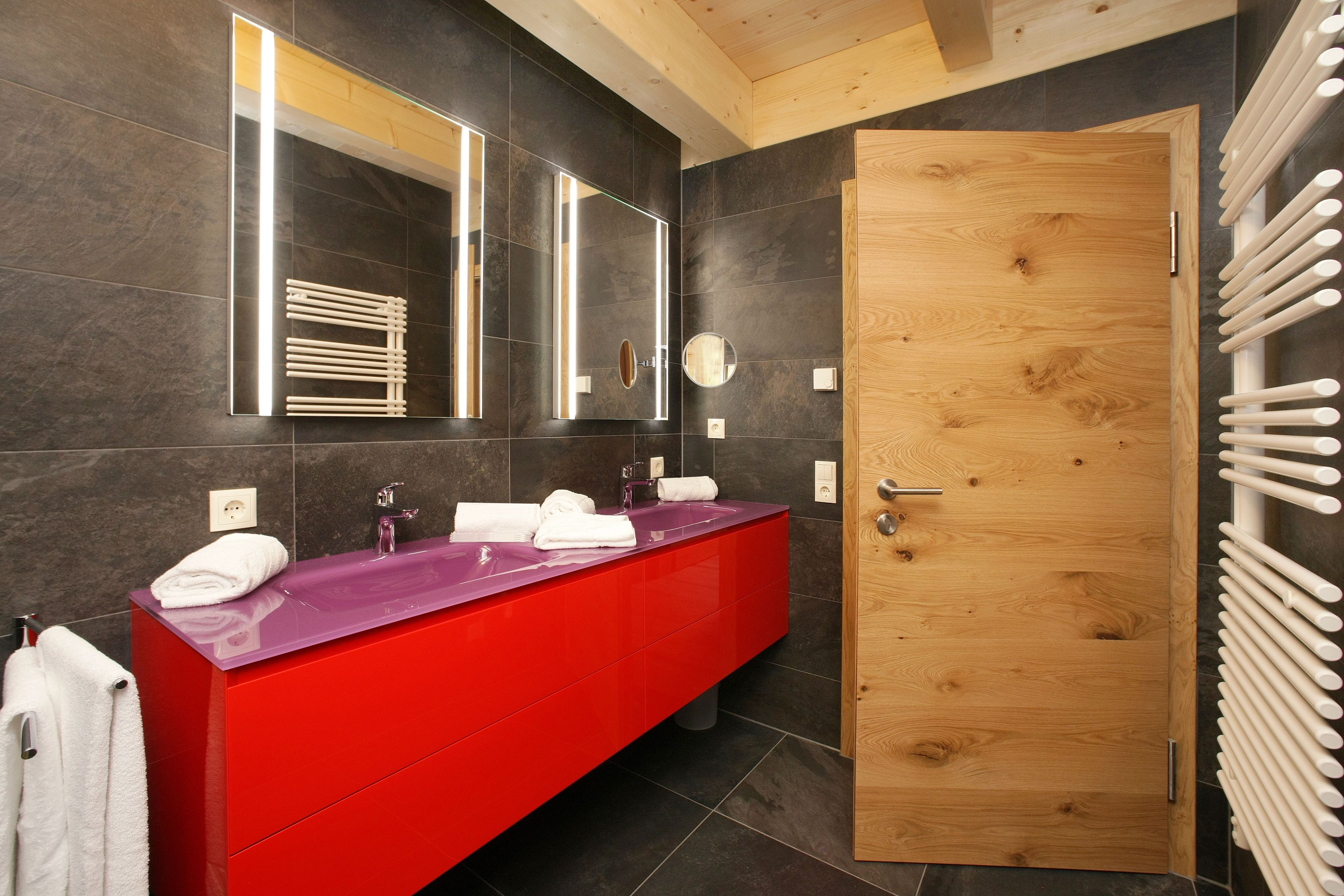 Un baño moderno con un tocador rojo, un espejo grande y una puerta de madera.