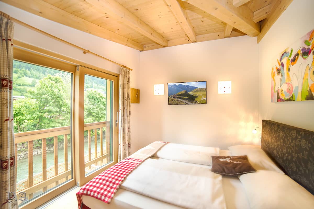 A bedroom with a bed, a window with a view of greenery, and a painting on the wall.