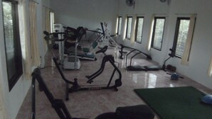 Un gimnasio con equipo de ejercicio, una colchoneta verde y ventanas amplias.