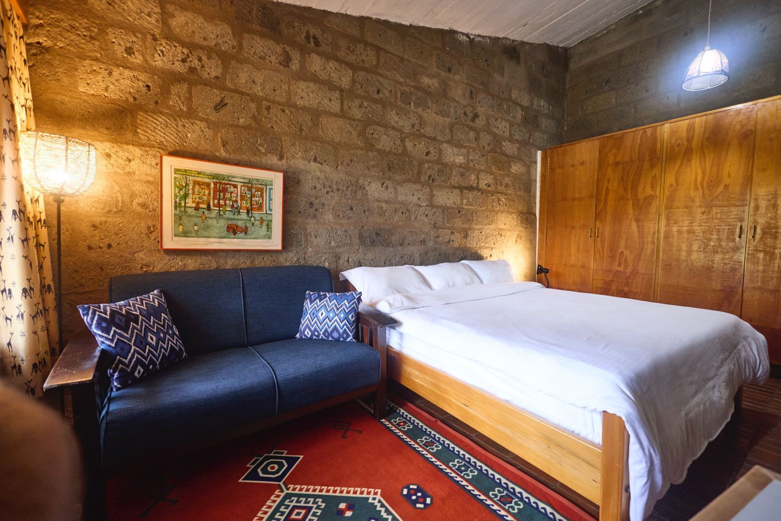 Una habitación con una cama, un sofá, un tapete, un armario de madera y un cuadro en la pared.