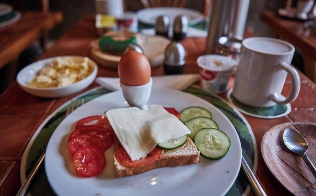 Prato de café da manhã com ovos, tomates, pepinos e queijo sobre torradas.