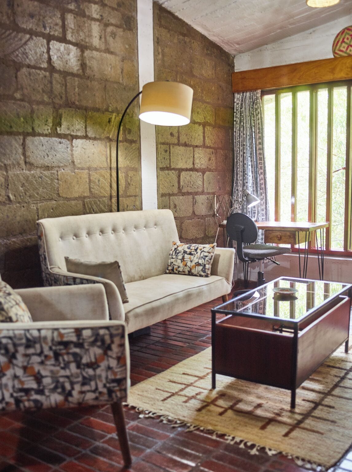 A room with a stone wall, a sofa, a patterned armchair, a coffee table, and a lamp.