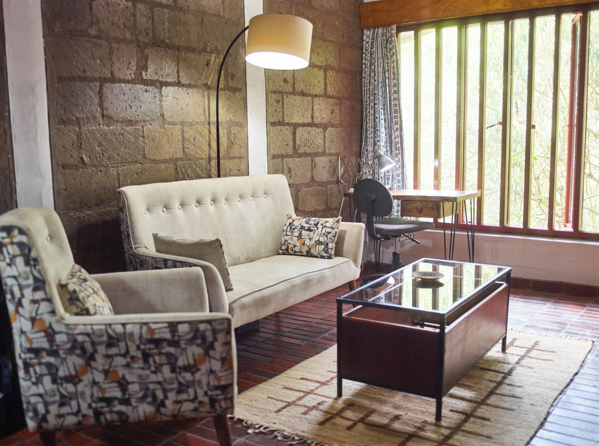 A living room with a sofa, armchair, and coffee table, a lamp, and a window with blinds.
