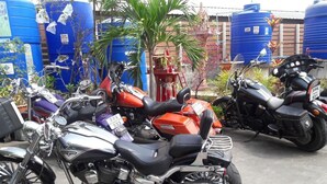 Una fila di motociclette parcheggiate all'aperto, con serbatoi d'acqua blu sullo sfondo.