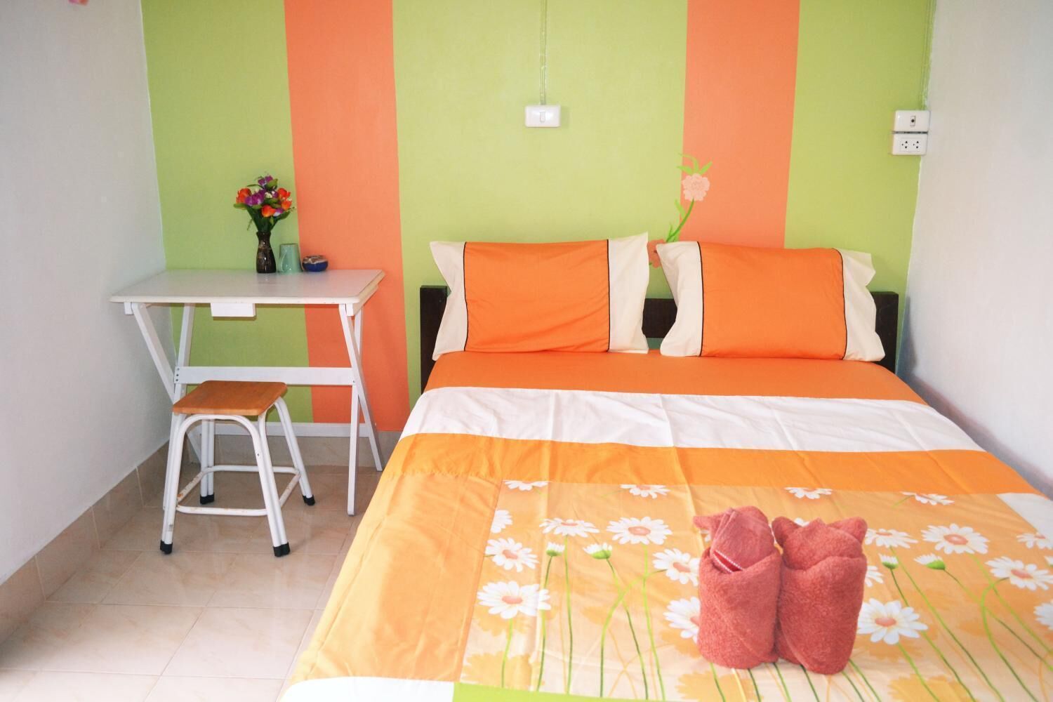 Ein Zimmer mit einem Bett, einem Schreibtisch und einem Stuhl. Auf dem Schreibtisch steht eine Vase mit Blumen.