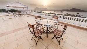 Une terrasse avec une table dressée pour le repas, un espace salon couvert et une vue sur une étendue d’eau, avec des montagnes en arrière-plan.