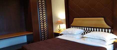 A hotel room with a large bed, a TV, and a nightstand with a lamp.