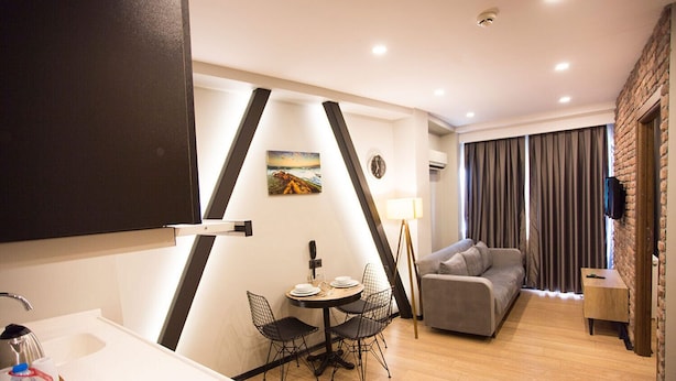 A modern living room with a sofa, a dining table with chairs, a kitchen area with a sink, and a large window with curtains. - Long Stay İstanbul (Taksim - Beyoglu - Istanbul)