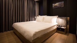 A modern hotel room with a large bed, dark curtains, a nightstand with a lamp, and a painting on the wall. - Long Stay İstanbul (Taksim - Beyoglu - Istanbul)