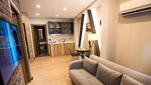 A modern living room with a sofa, a TV mounted on a brick wall, a kitchen area with wooden cabinets, and a dining table with chairs. - Long Stay İstanbul (Taksim - Beyoglu - Istanbul)