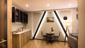 A compact kitchen with wooden cabinets, a dining table with chairs, a clock, and a lamp. - Long Stay İstanbul (Taksim - Beyoglu - Istanbul)