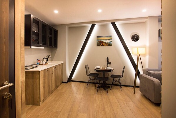 A compact kitchen with wooden cabinets, a dining table with chairs, a clock, and a lamp. - Long Stay İstanbul (Taksim - Beyoglu - Istanbul)
