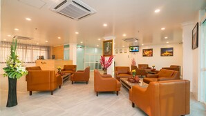 A hotel lobby with leather sofas, a reception desk, and a TV on the wall. - Sakura Hotel (Yangon)
