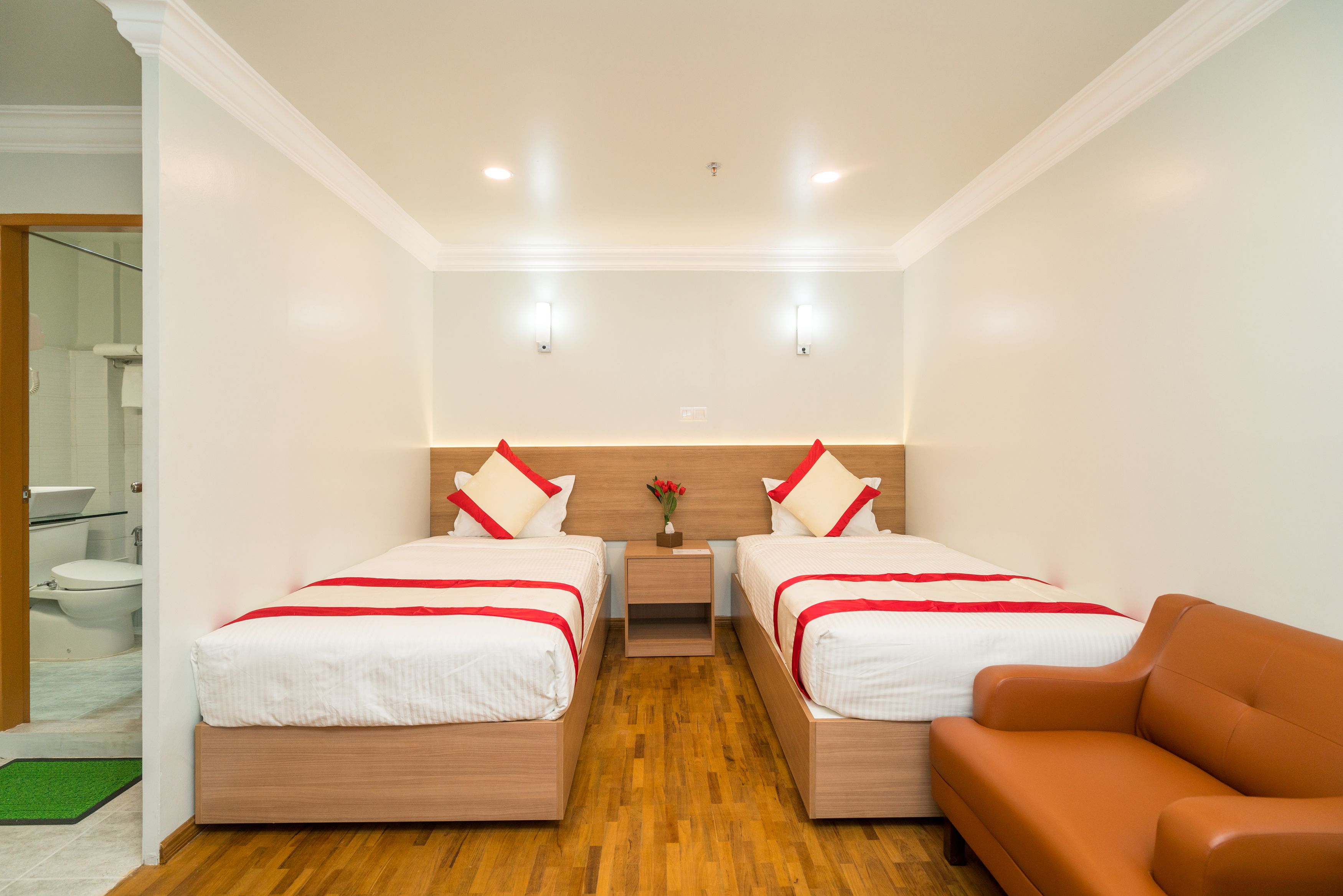 A hotel room with two beds, a wooden floor, a brown sofa, and a small table with a vase.