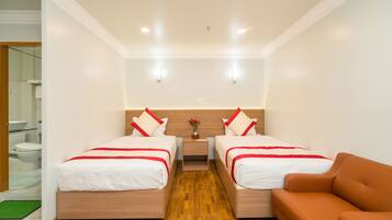 A hotel room with two beds, a wooden floor, a brown sofa, and a small table with a vase.