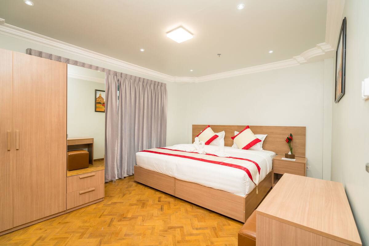 A bedroom with a large bed, wooden wardrobe, a desk, and a nightstand.