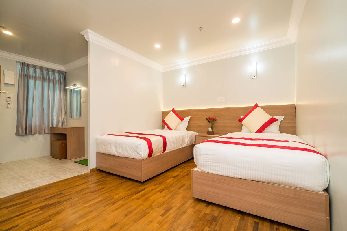 A hotel room with two beds, wooden flooring, a small bedside table, a nightstand, and a mirror.